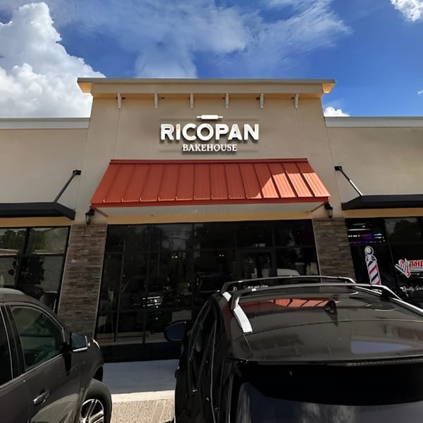 Ricopan Bakehouse storefront with a red awning, large windows, and cars parked in front.