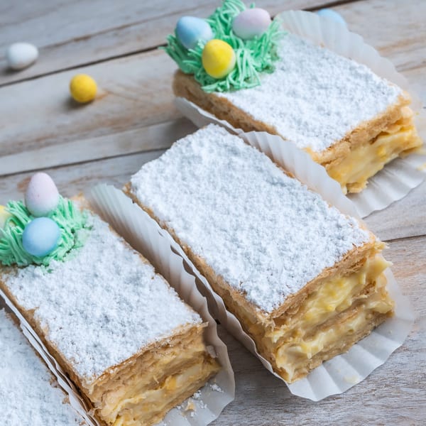 Three rectangular pastries with powdered sugar, two decorated with green frosting and colorful candy eggs.