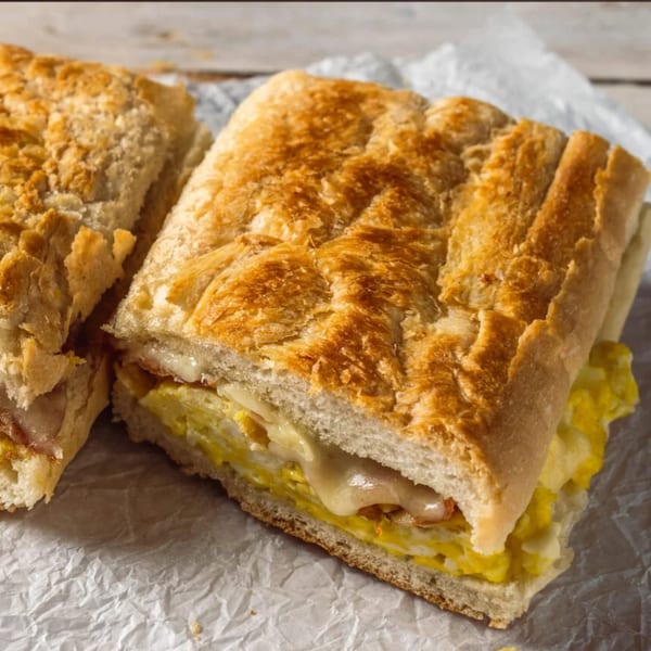 A golden-brown toasted sandwich, cut in half, revealing melted cheese and yellow scrambled eggs.