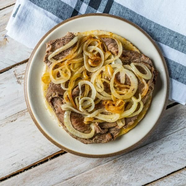 A plate of steak with sautéed onions on a rustic wooden table with a striped napkin.