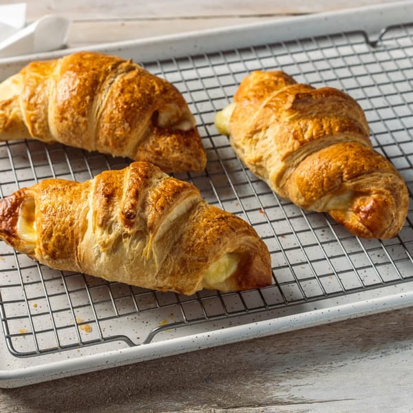 Three golden-brown croissants, two with visible cheese filling, resting on a cooling rack.