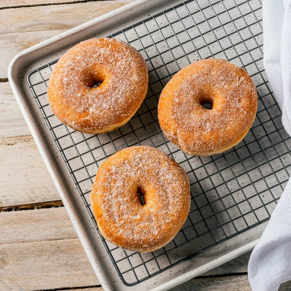Three sugar-dusted donuts on a cooling rack, with a white napkin and wooden surface.