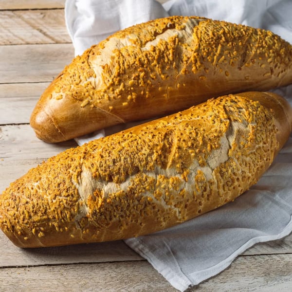Two golden-brown loaves of bread, topped with crunchy cheese, resting on a white cloth and wooden table.