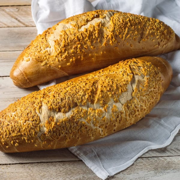 Two golden-brown loaves of bread with a crispy, textured topping on a white cloth and wooden table.