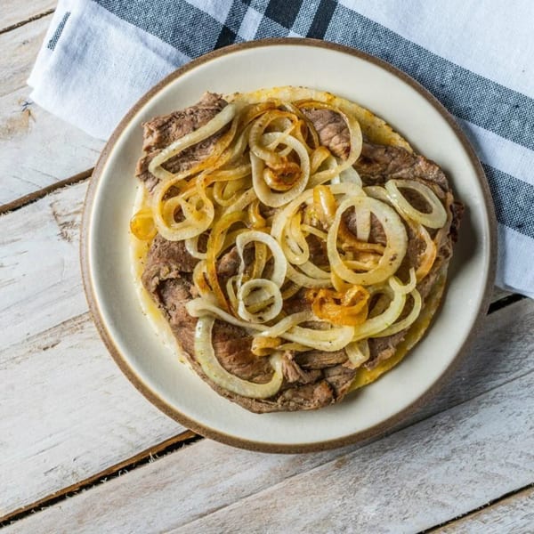 A plate of steak with sautéed onions on a white wooden table with a striped napkin.