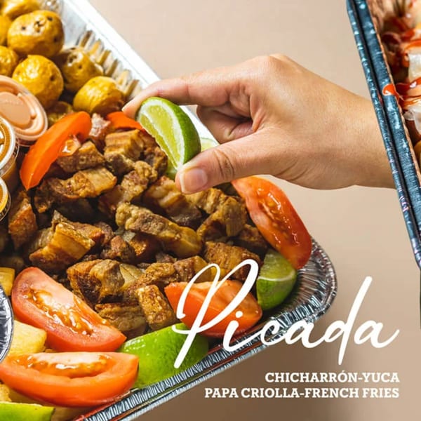 A hand squeezing lime over a tray of chicharrón, tomatoes, and potatoes.