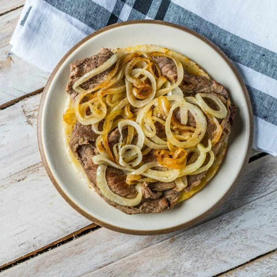 A plate of steak and onions on a white wooden table with a striped napkin.