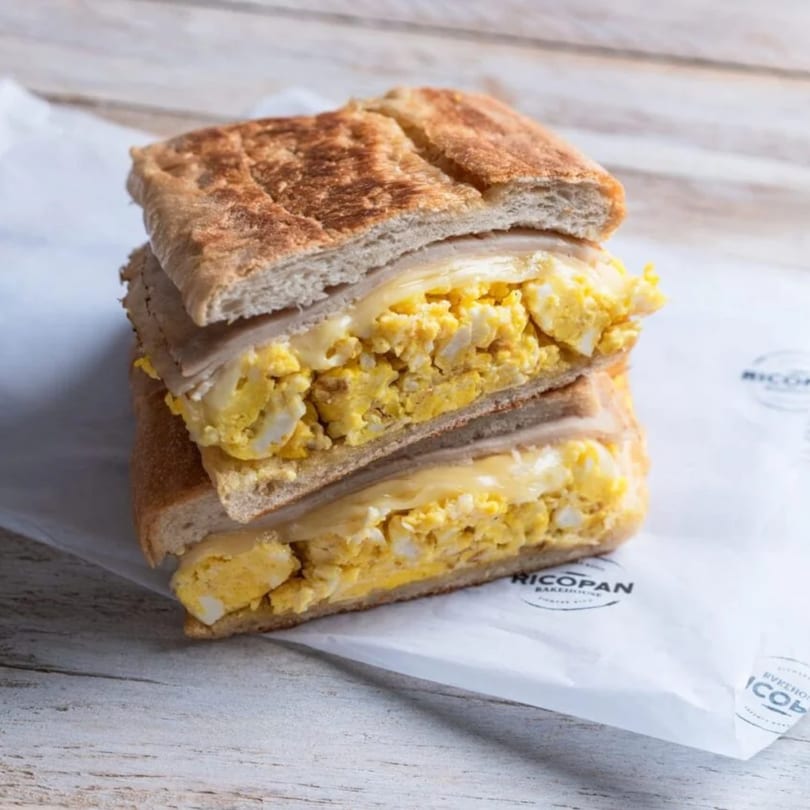 A stacked breakfast sandwich with scrambled eggs and melted cheese on toasted bread.