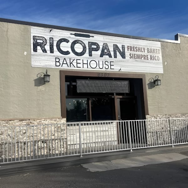 Ricopan Bakehouse storefront with a white sign, dark windows, and a metal fence in front.