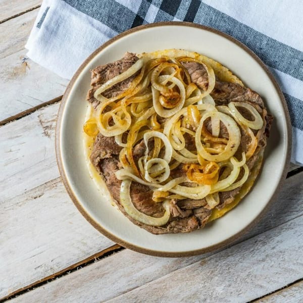A plate of steak with sautéed onions on a white wooden table with a striped napkin.