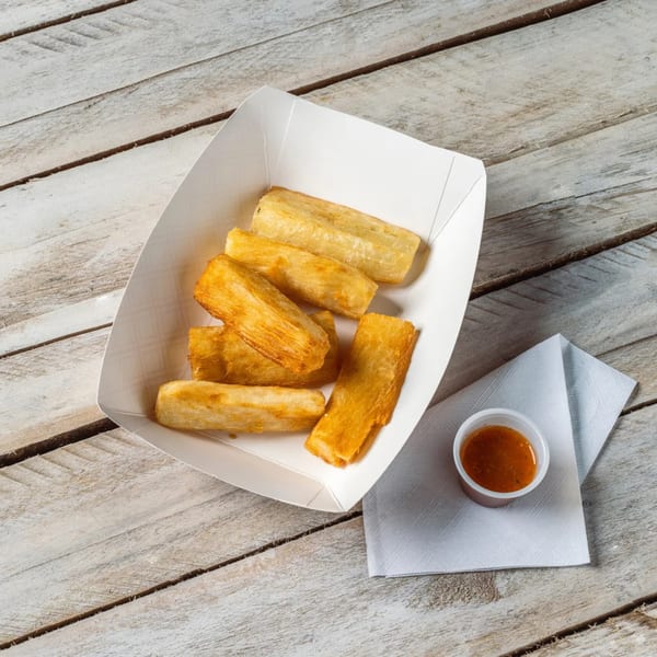 Golden-brown fried yuca sticks in a white paper tray with a side of dipping sauce.