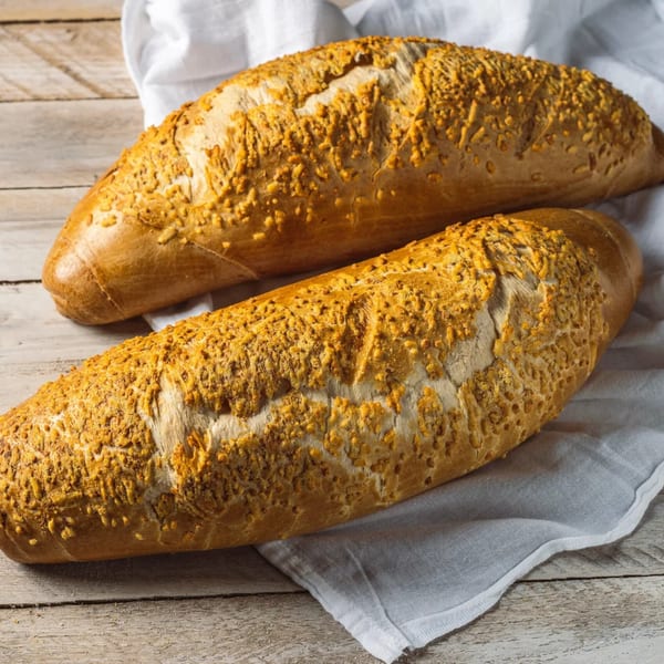 Two golden-brown baguettes with a crispy, cheesy topping rest on a white cloth and wooden table.