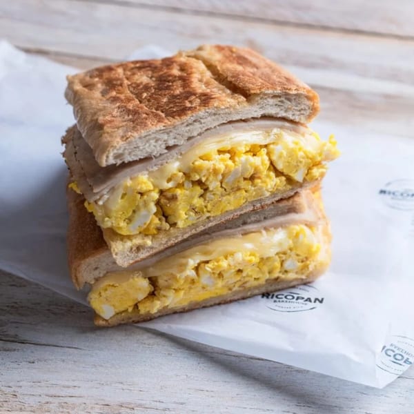 A toasted breakfast sandwich with scrambled eggs and melted cheese, cut in half and stacked.