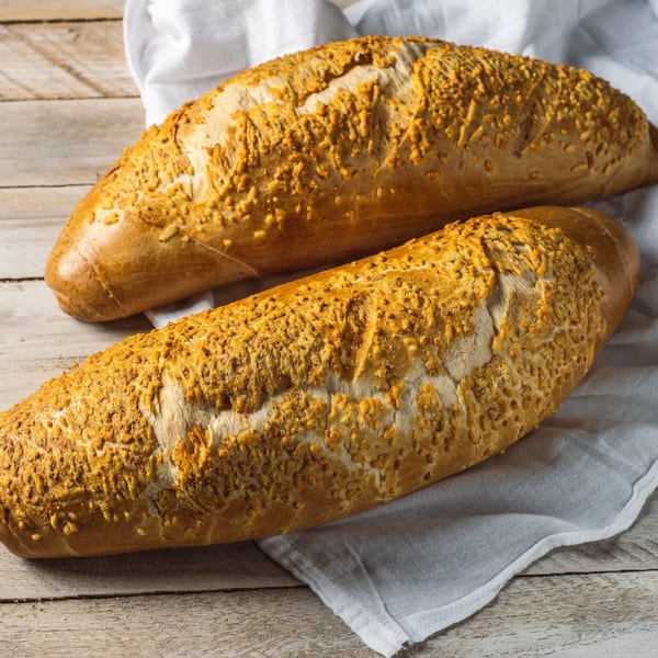 Two golden-brown baguettes with a crispy, cheesy topping rest on a white cloth and wooden table.
