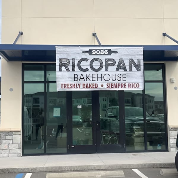 Ricopan Bakehouse sign hanging above the entrance of a new building with large glass windows.