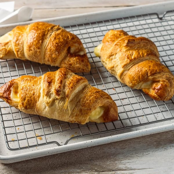 Three golden-brown croissants, two with visible cheese filling, rest on a cooling rack.